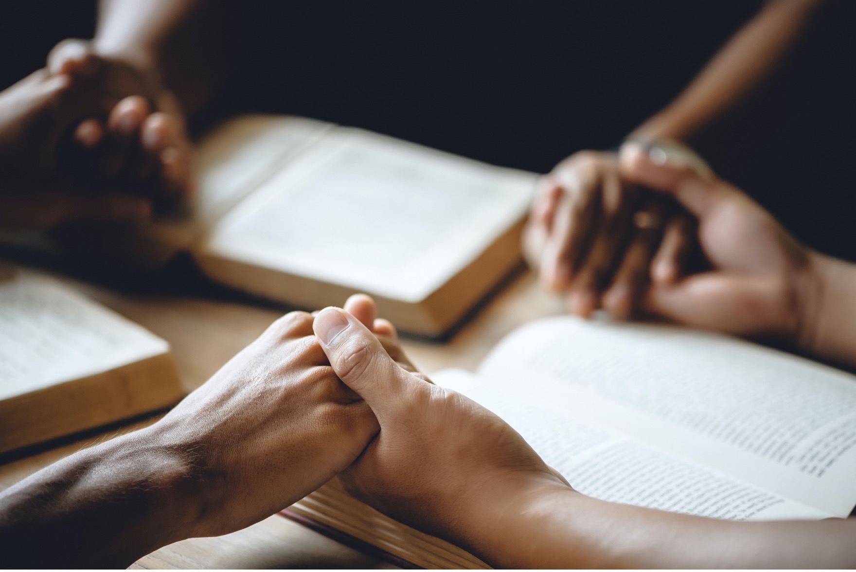 Holding hands in circle with Bibles in a Christian Bible study group.